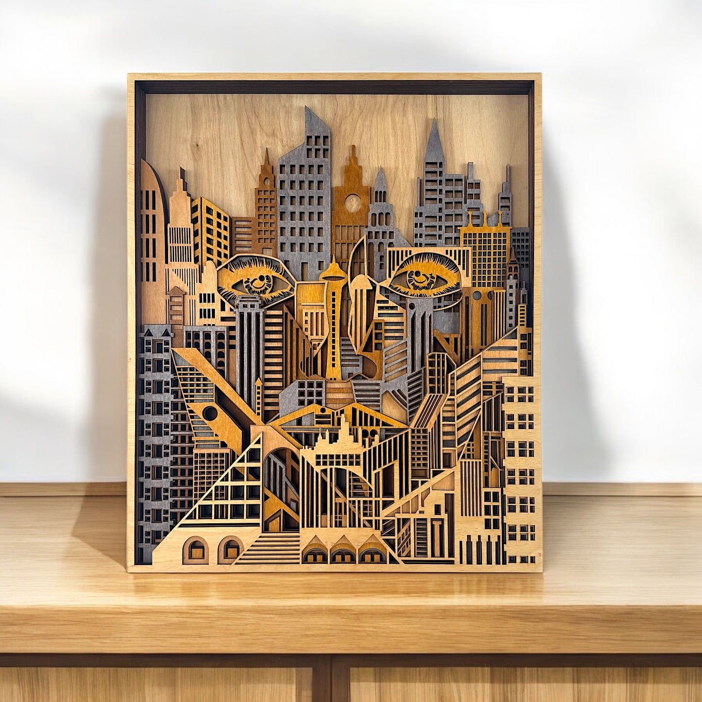 Laser-cut wooden face hidden within a detailed cityscape, displayed on a wooden shelf under soft lighting