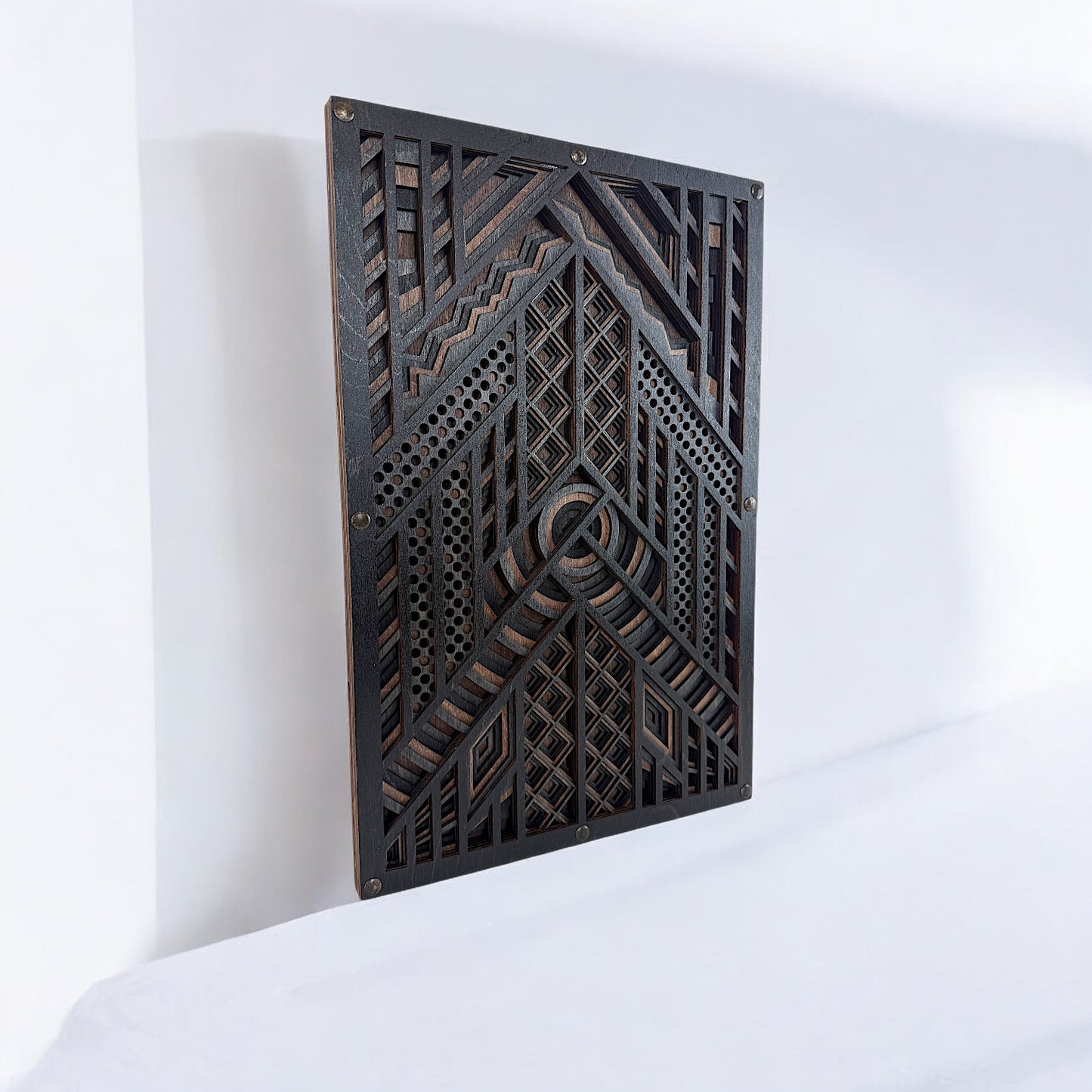 Laser-cut wood wall art displayed upright on a white surface, showing the layered design’s depth and complex geometric detailing in dark wood tones.