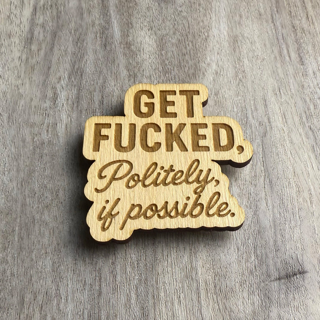 Angled view of a laser-cut wooden magnet featuring the phrase Get Fucked, Politely, if possible in mixed fonts, highlighting the engraved depth and material layering on a gray wood surface.