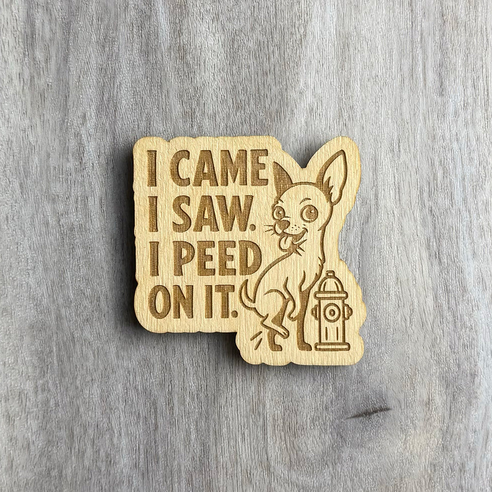 Laser-cut wooden magnet engraved with the phrase I Came I Saw I Peed On It, featuring a cartoon chihuahua lifting its leg next to a fire hydrant, displayed on a gray wood background.