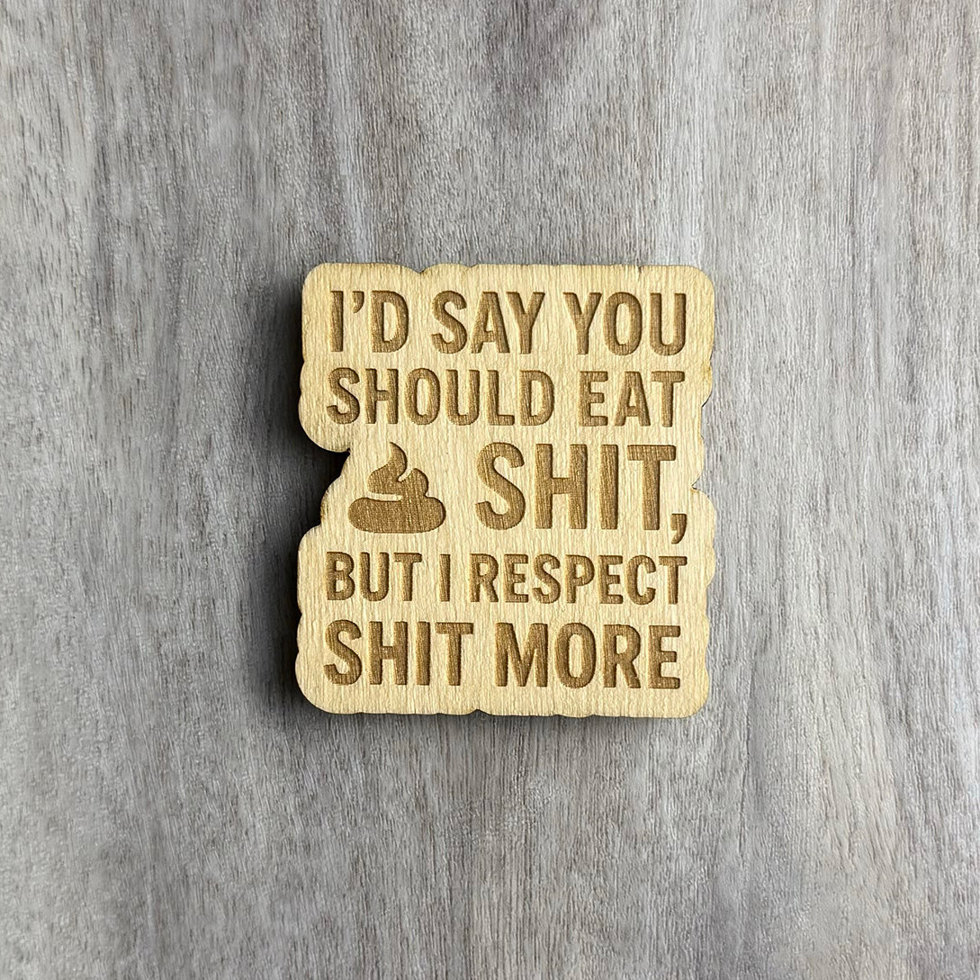 Laser-engraved wooden magnet featuring the phrase “I’D SAY YOU SHOULD EAT SHIT, BUT I RESPECT SHIT MORE” in bold capital letters, with a poop emoji engraved before the word "SHIT." The magnet has a wavy cutout border and is placed on a woodgrain background.