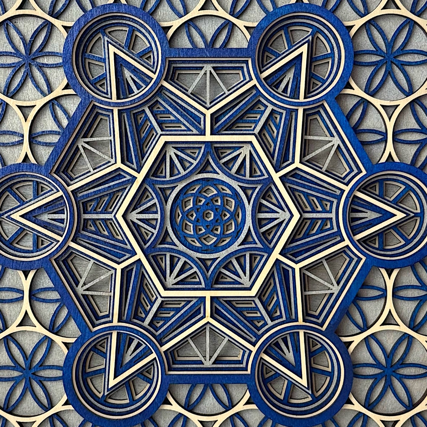 Close-up of the central pattern in "Metatron Ascend" showing the fine laser-cut detail in blue, gray, and natural wood tones.