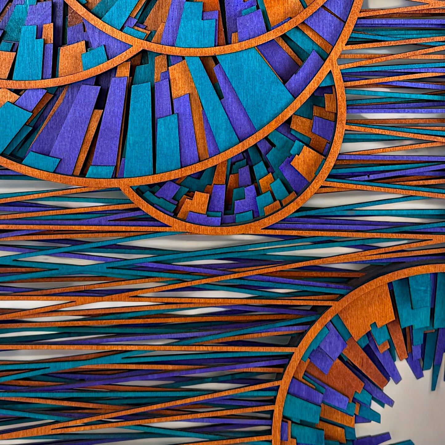 Macro view of the bottom portion of the wood art, capturing overlapping diagonal wood strips and tight angular compositions in rich purple, teal, and orange shades.