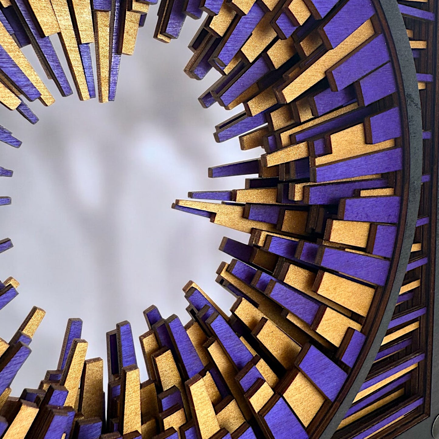 Macro detail of laser-cut birch layers in Metrorhythm V1, revealing intricate interlocking shapes and vibrant hand-dyed color.
