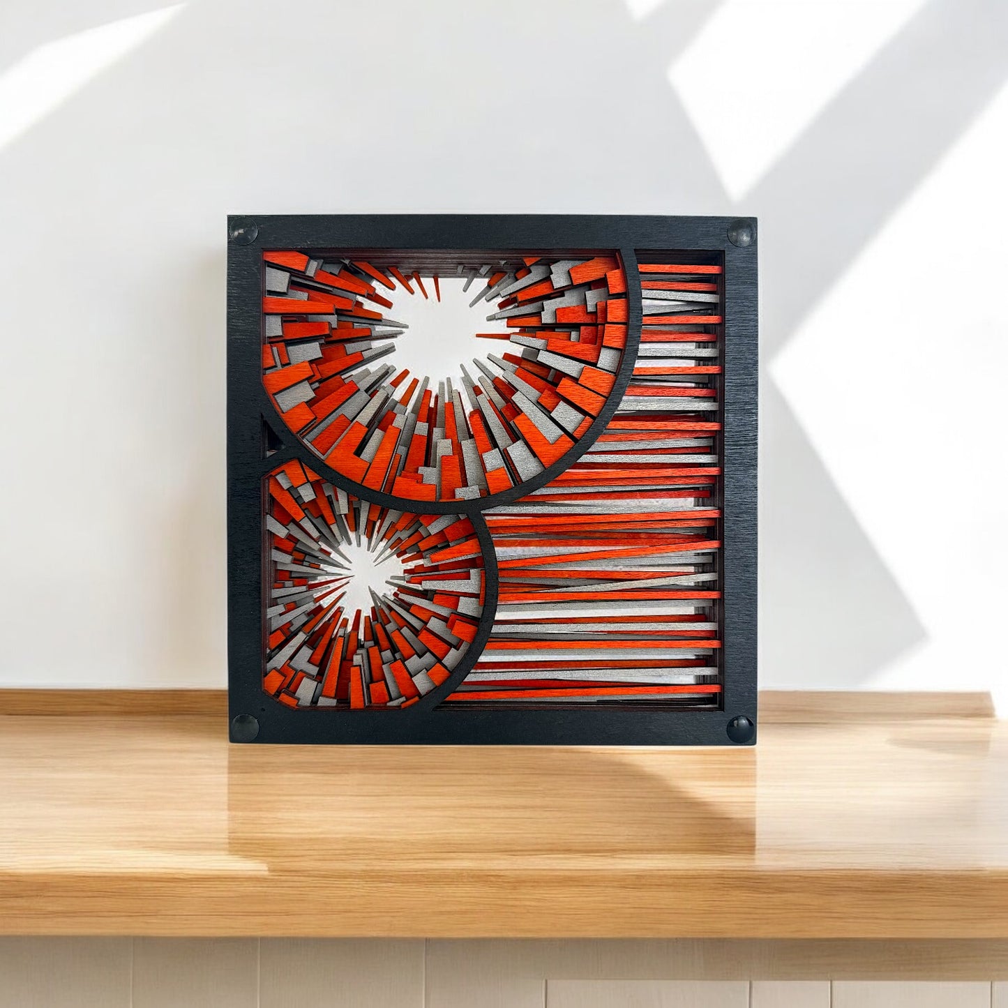 Freestanding wood sculpture displayed on a light wood surface, showing bold radial bursts and linear texture.