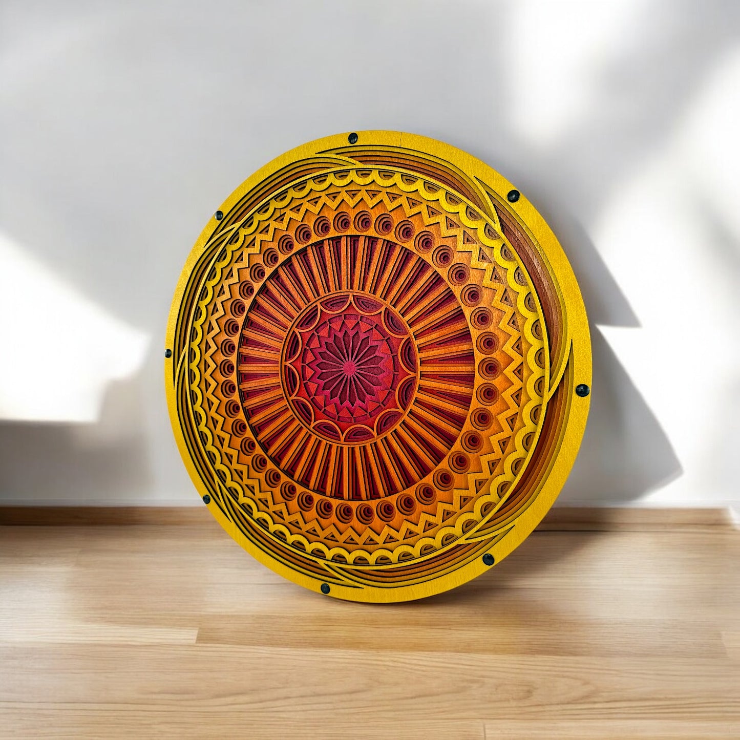Orbit Array mandala placed on a wood floor against a white wall, natural light casting soft shadows across its vivid yellow and orange surface.