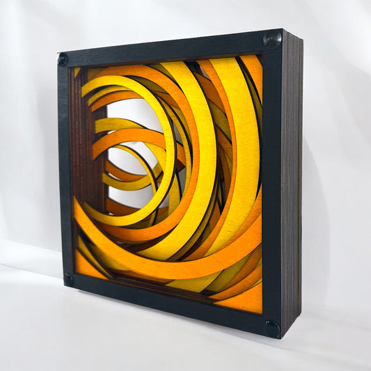 Angled view of Radiant Drift layered wood artwork showing its dimensional structure and vibrant circular movement in yellow-orange hues.