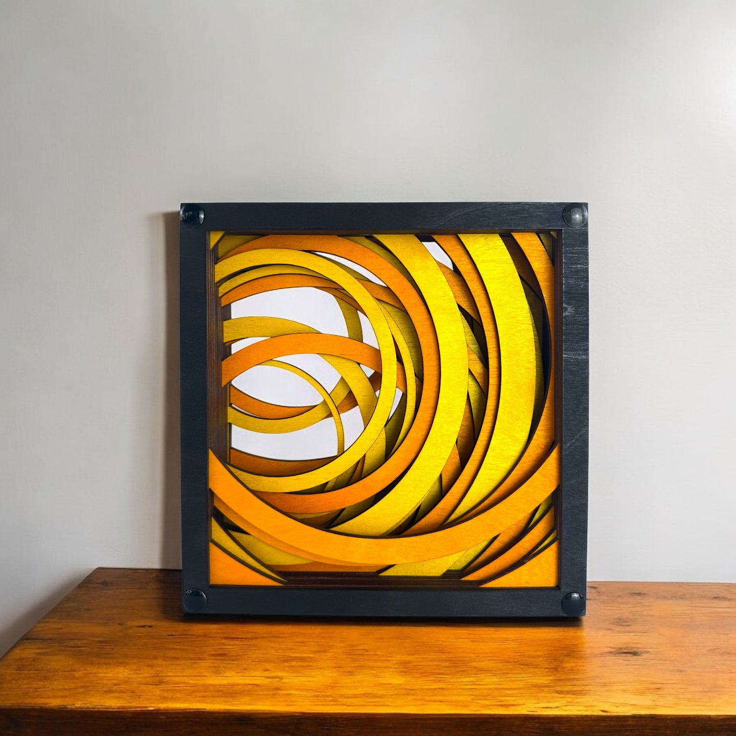 Radiant Drift laser-cut wood art sitting on a wooden surface, emphasizing its vibrant sunburst-inspired curves within a black frame.