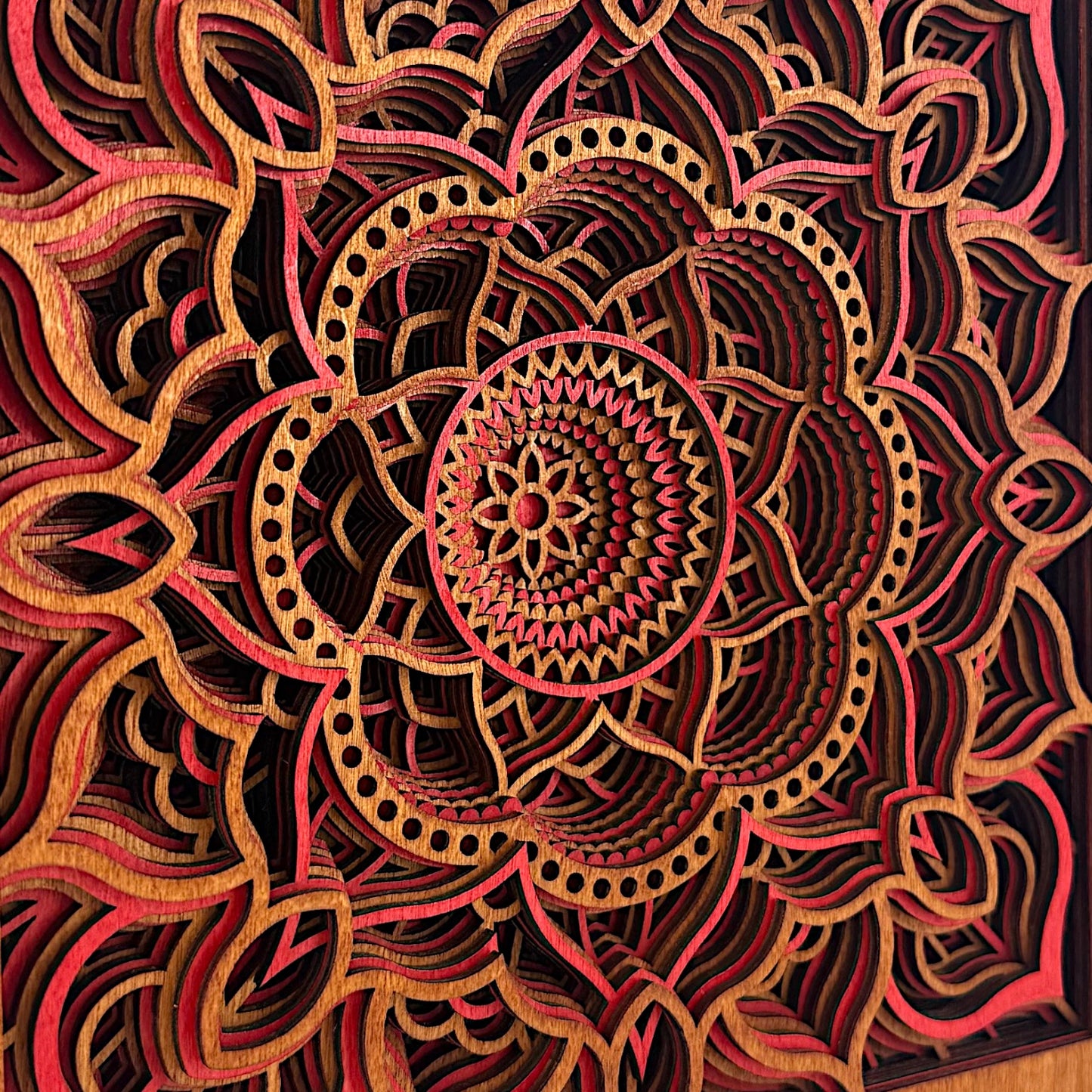 Angled macro shot of Temple Bloom mandala art showing laser precision and stacked layers in vivid red and amber tones.