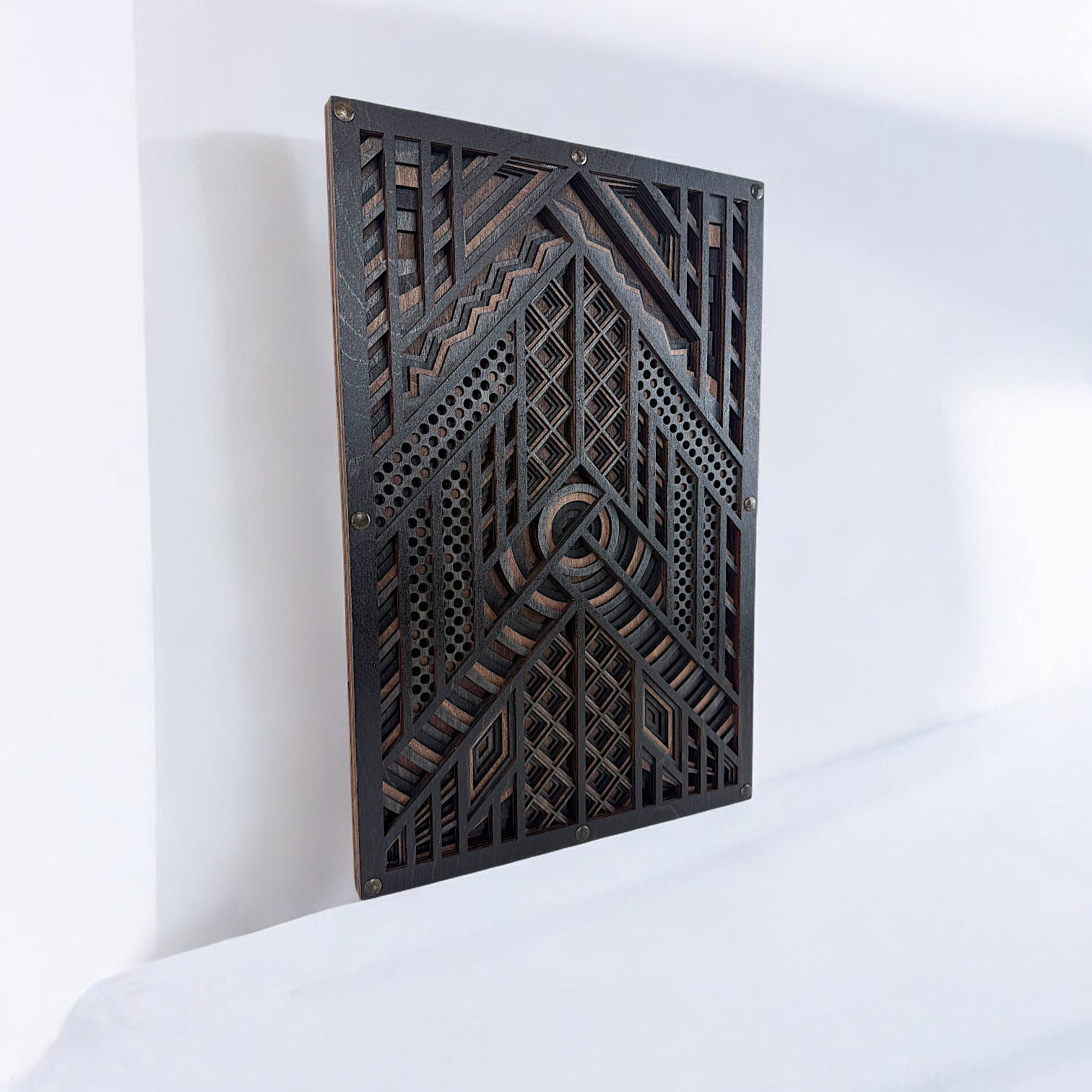Laser-cut wood wall art displayed upright on a white surface, showing the layered design’s depth and complex geometric detailing in dark wood tones.
