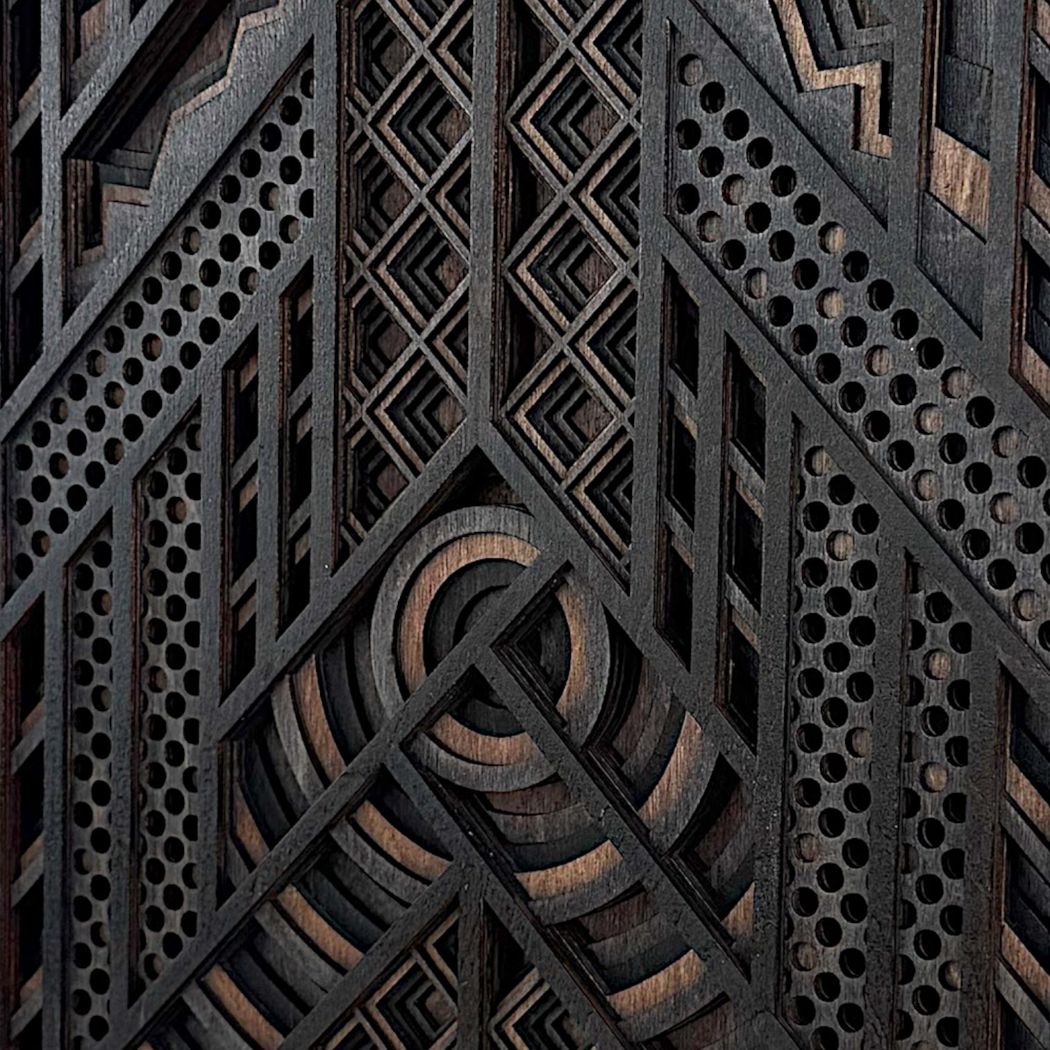 Detailed macro shot of a geometric laser-cut wood artwork, highlighting the layered circular centerpiece, diamond motifs, and perforated accents.