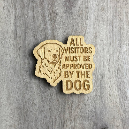 Laser-cut wooden magnet featuring an engraved illustration of a golden retriever on the left and the text 'ALL VISITORS MUST BE APPROVED BY THE DOG' on the right, displayed on a gray wood background.