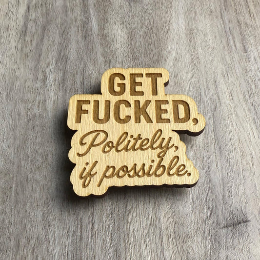 Angled view of a laser-cut wooden magnet featuring the phrase Get Fucked, Politely, if possible in mixed fonts, highlighting the engraved depth and material layering on a gray wood surface.