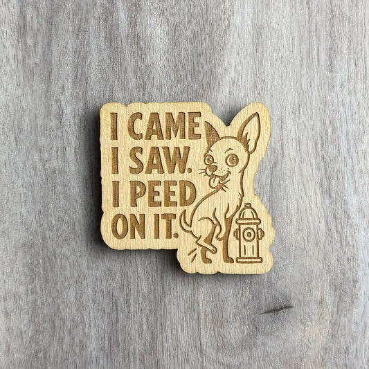 Laser-cut wooden magnet engraved with the phrase I Came I Saw I Peed On It, featuring a cartoon chihuahua lifting its leg next to a fire hydrant, displayed on a gray wood background.