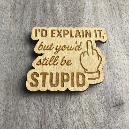 Angled view of the same laser-engraved wooden magnet showing the phrase “I’d explain it, but you’d still be STUPID” with a middle finger hand illustration. The lighting emphasizes the engraved depth and wood grain texture.