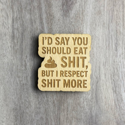 Laser-engraved wooden magnet featuring the phrase “I’D SAY YOU SHOULD EAT SHIT, BUT I RESPECT SHIT MORE” in bold capital letters, with a poop emoji engraved before the word "SHIT." The magnet has a wavy cutout border and is placed on a woodgrain background.