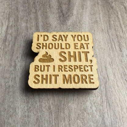 Angled view of a wooden magnet engraved with the phrase “I’D SAY YOU SHOULD EAT SHIT, BUT I RESPECT SHIT MORE.” The lighting highlights the engraved depth and natural texture of the wood.