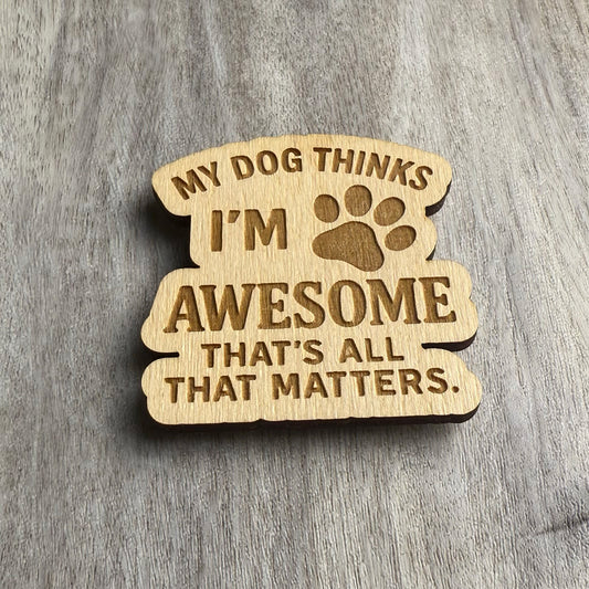 Angled view of the same engraved wooden magnet that reads “MY DOG THINKS I’M AWESOME THAT’S ALL THAT MATTERS,” with a paw print illustration integrated into the design. The woodgrain and engraved details are enhanced by directional lighting.