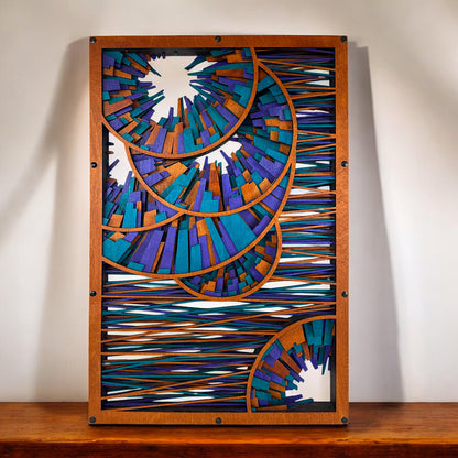 Wood wall art displayed above a wooden surface, centered and well-lit, showing crisp outlines of nested spirals in a burst-like pattern with horizontal color-threaded accents.