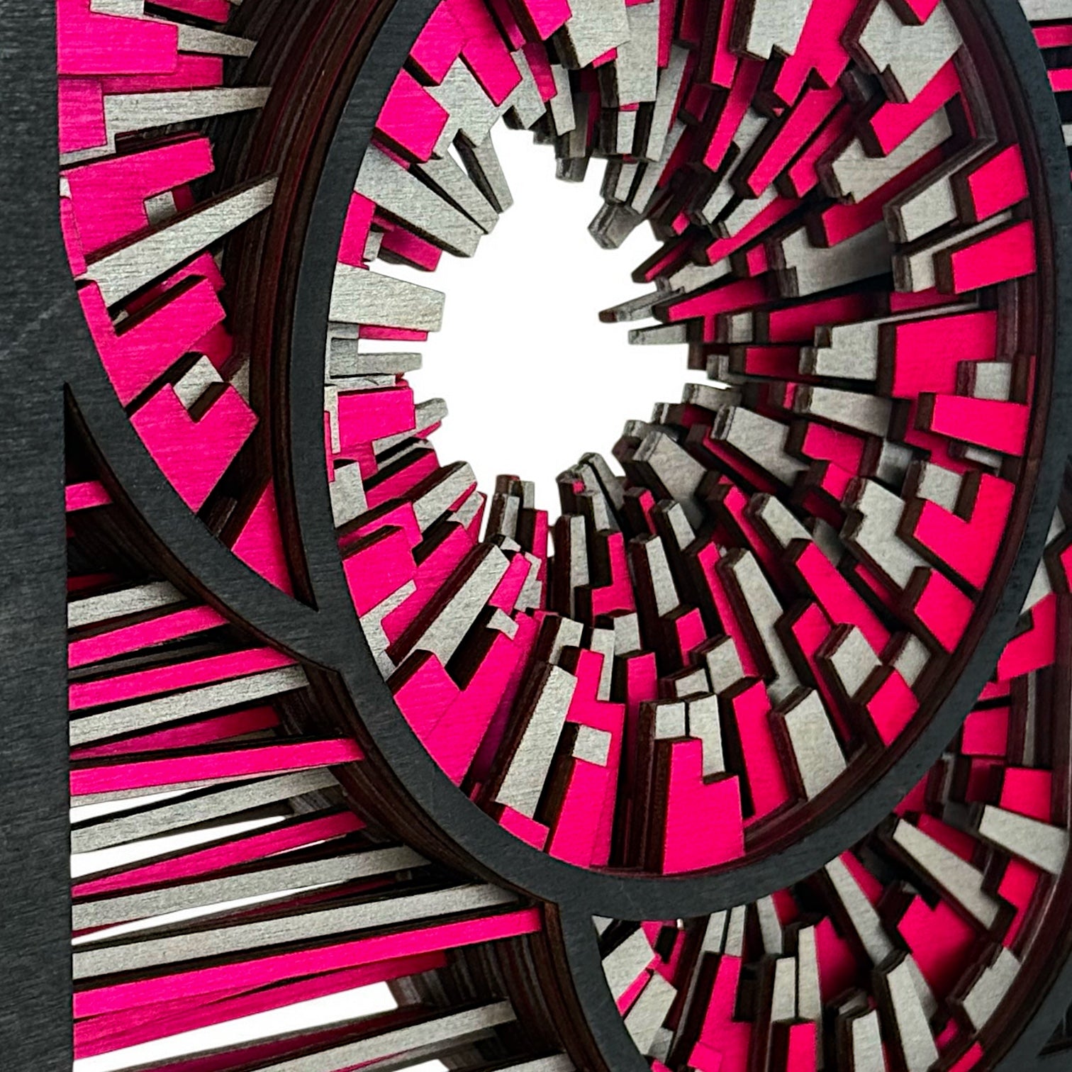 Detailed macro of layered wooden segments in silver and vibrant pink, revealing the texture and depth of the radial form.